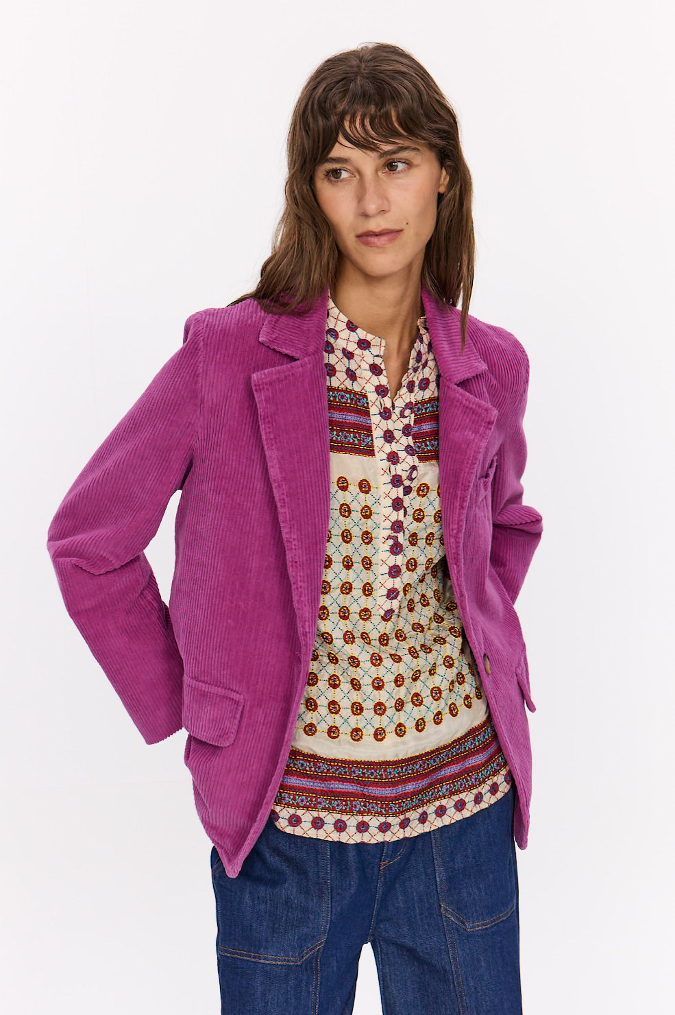  Veste Velvet fuchsia portée ouverte, avec col tailleur et poches à rabat, sur une tunique imprimée.