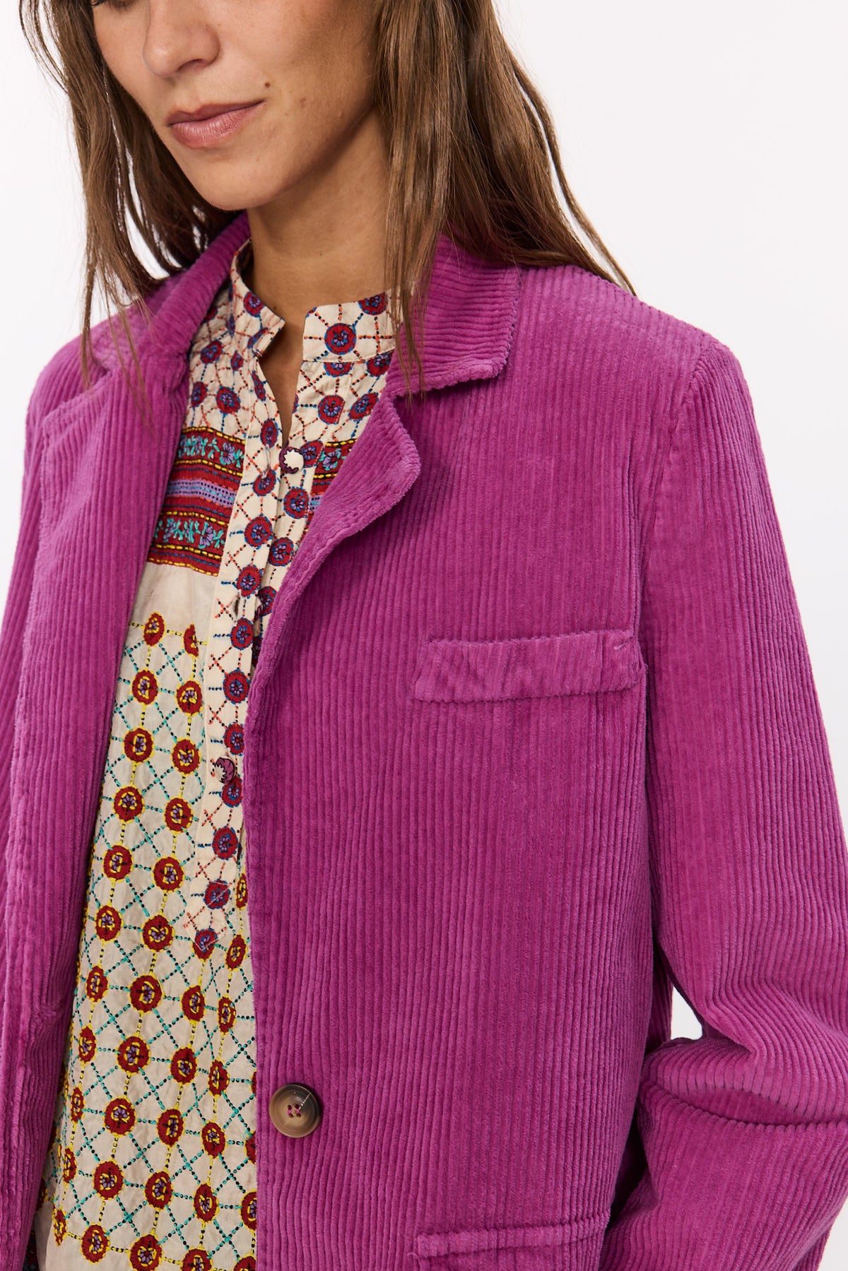 Gros plan sur le velours côtelé fuchsia de la veste Velvet, son col tailleur, sa poche poitrine et son bouton.